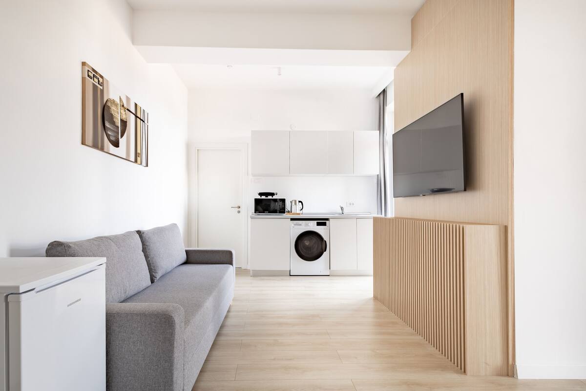 A modern kitchen with a washing machine, a microwave, and a flat-screen TV mounted on the wall.