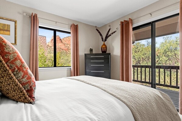 Relax in this serene retreat with a large bed, dresser, and scenic views of a red rock formation and lush greenery.