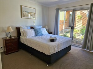 A bedroom with a large bed, two bedside tables, a nightstand, a framed picture on the wall, and a sliding glass door leading to an outdoor area. - "Sunshine On The Water" Absolute Waterfront & Jetty.  Paradise at your doorstep. (Sunshine)