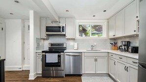 A modern kitchen with stainless steel appliances, white cabinetry, and a window providing natural light. - Entire 4-Bedroom Garden Level Suite Near UBC/YVR (Vancouver)