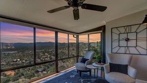 A room with large windows offering a city view, a ceiling fan, and a modern chair.