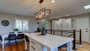 A modern kitchen with a central island, white cabinetry, and a dining area with black chairs.
