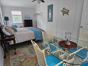 A bedroom with a bed, a dresser, a chair, a table, and a ceiling fan. - Starry Night Cottage • Bayfront • Pet Friendly • Fenced Yard • Sleeps 4 (Eastpoint)