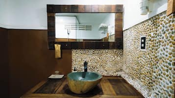 Un baño con un lavabo de piedra, tocador de madera y espejo con marco de madera.