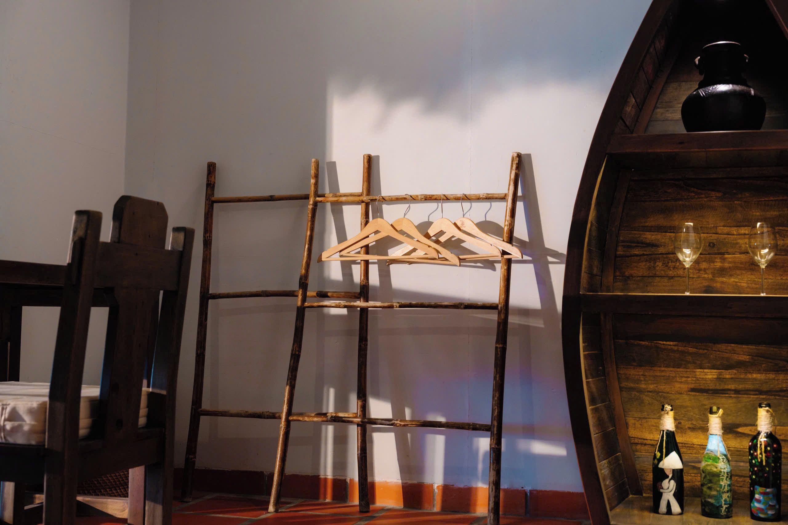 Ein rustikaler Innenraum mit einem Holzgestell für Kleidung, einem Holzstuhl und einer Ablagefläche mit Weinflaschen und Gläsern.