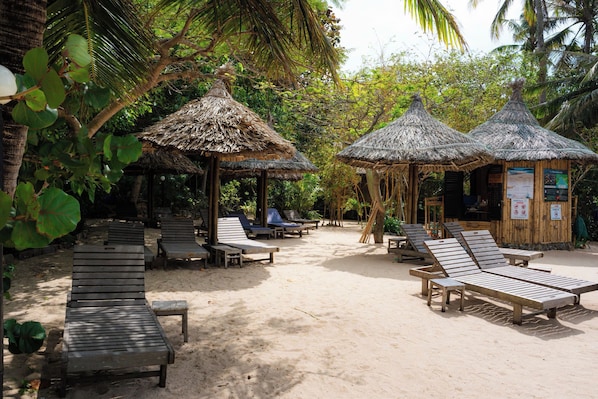 A beachside area with thatched-roof huts, wooden lounge chairs, and a sandy ground. - Whale Island Resort (Nha Trang)