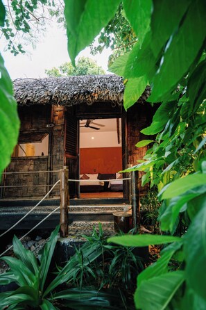 A rustic wooden structure with a thatched roof, a bed, and a small staircase leading to a door. - Whale Island Resort (Nha Trang)