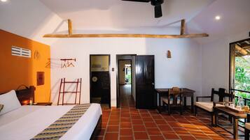 Habitación de hotel con cama, escritorio y silla. Cuenta con ventilador de techo y ventana con vista a follaje.