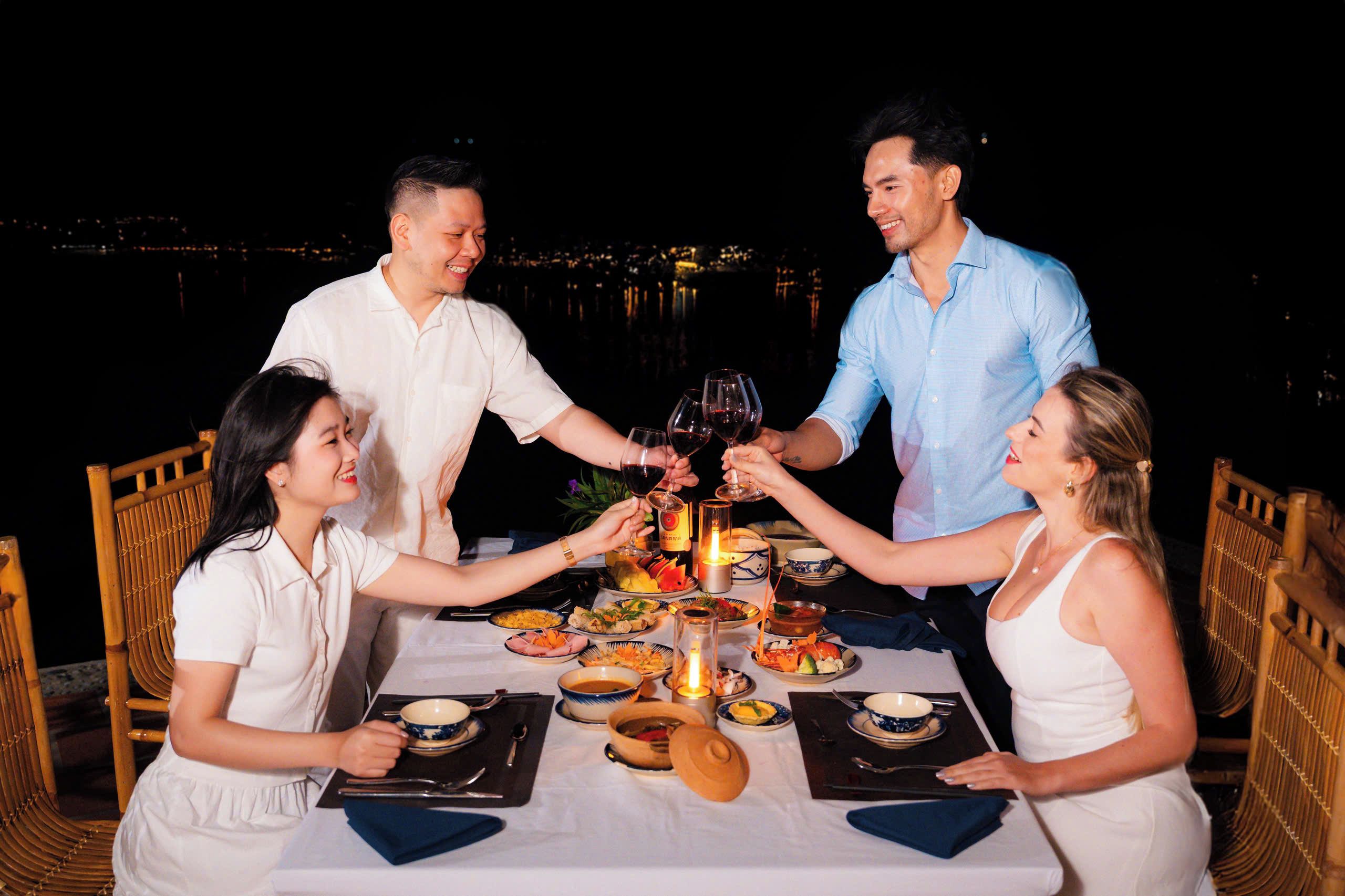 Um grupo de pessoas brindando à mesa de jantar com vista para a cidade à noite.