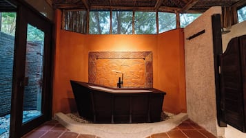 Um banheiro com uma banheira de apoio, um detalhe decorativo na parede e uma janela com vista para árvores.