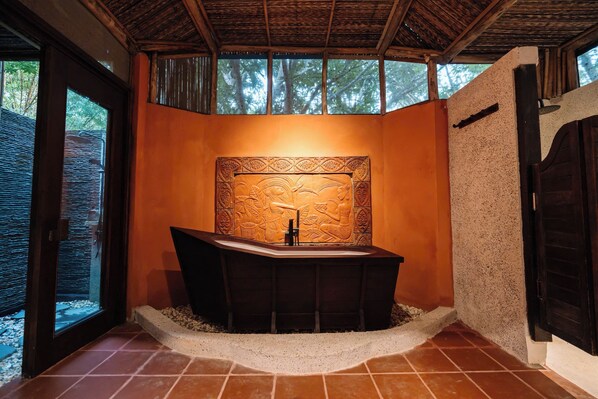 A bathroom with a freestanding bathtub, a decorative wall, and a window with a view of trees.
