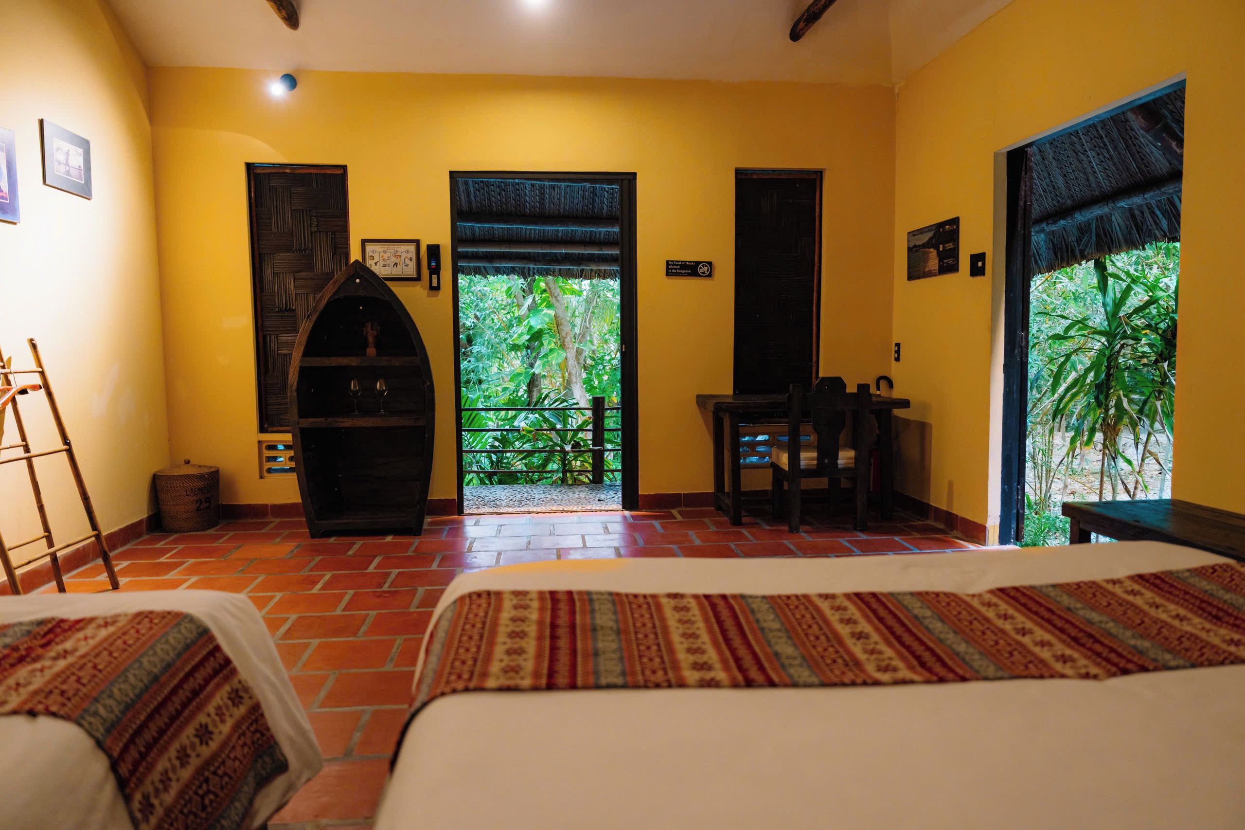 Habitación con dos camas, un escritorio y vista a zonas verdes por una puerta.