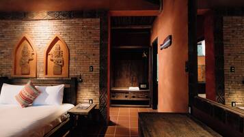 A room with a brick wall, a bed with a patterned pillow, a wooden bench, and a small table.