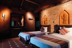 Habitación de hotel con dos camas, pared de ladrillo con adornos, cabecera de madera y suelo de baldosas.