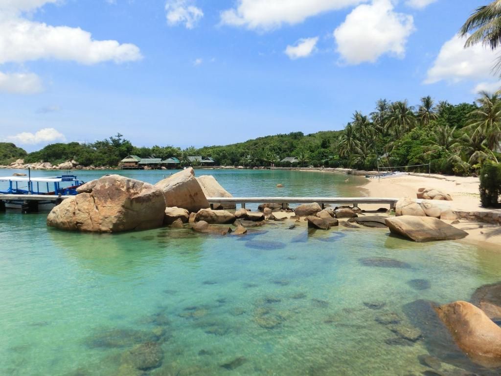 A clear tropical beach with a dock, rocks, and palm trees.