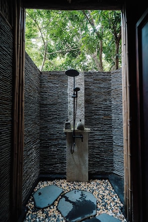 A modern shower area with a stone wall, bamboo elements, and a view of trees. - Whale Island Resort (Nha Trang)