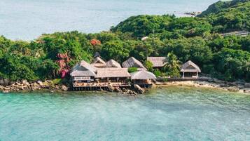 Un resort costero con bungalows sobre el agua, aguas turquesas cristalinas y abundante vegetación.