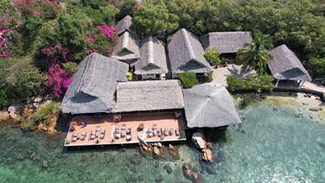 Vista aérea de un resort con edificios de techo de paja, agua turquesa cristalina y abundante vegetación.