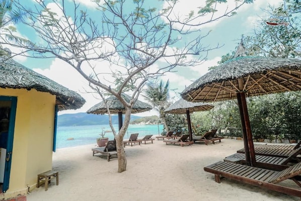 A beachside resort with thatched umbrellas, wooden lounge chairs, and a view of the sea. - Whale Island Resort (Nha Trang)
