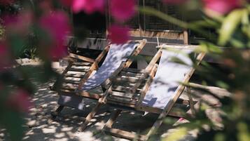 Three wooden lounge chairs with canvas backs, positioned on a sandy surface, surrounded by greenery.