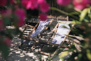 Three wooden lounge chairs with canvas backs, positioned on a sandy surface, surrounded by greenery. - Whale Island Resort (Nha Trang)