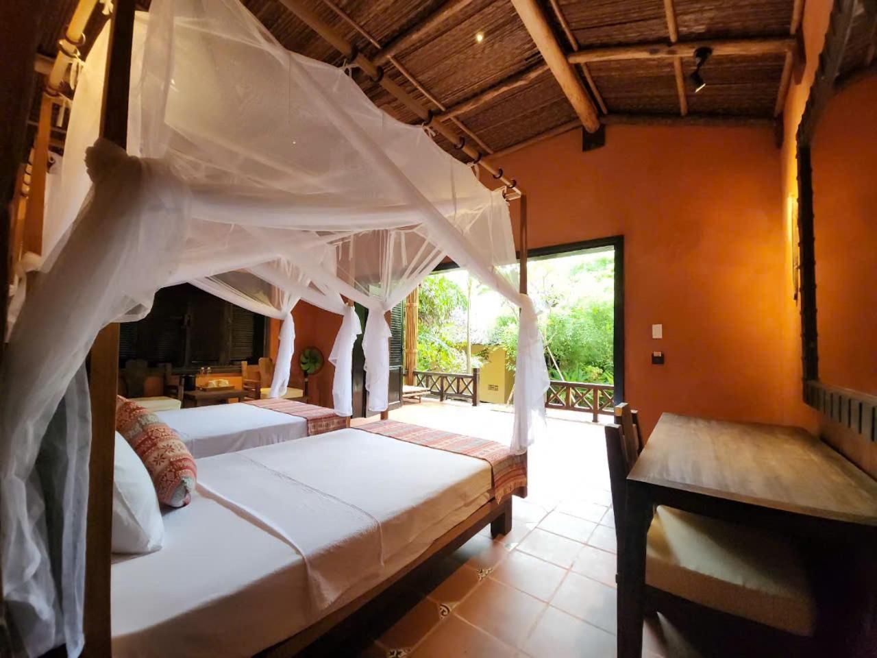 Habitación con cama bajo un dosel, una mesita y vistas al exterior.