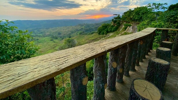 A wooden deck with a view of a sunset over a hilly landscape. - Altos de agua blanca  (Tauramena)