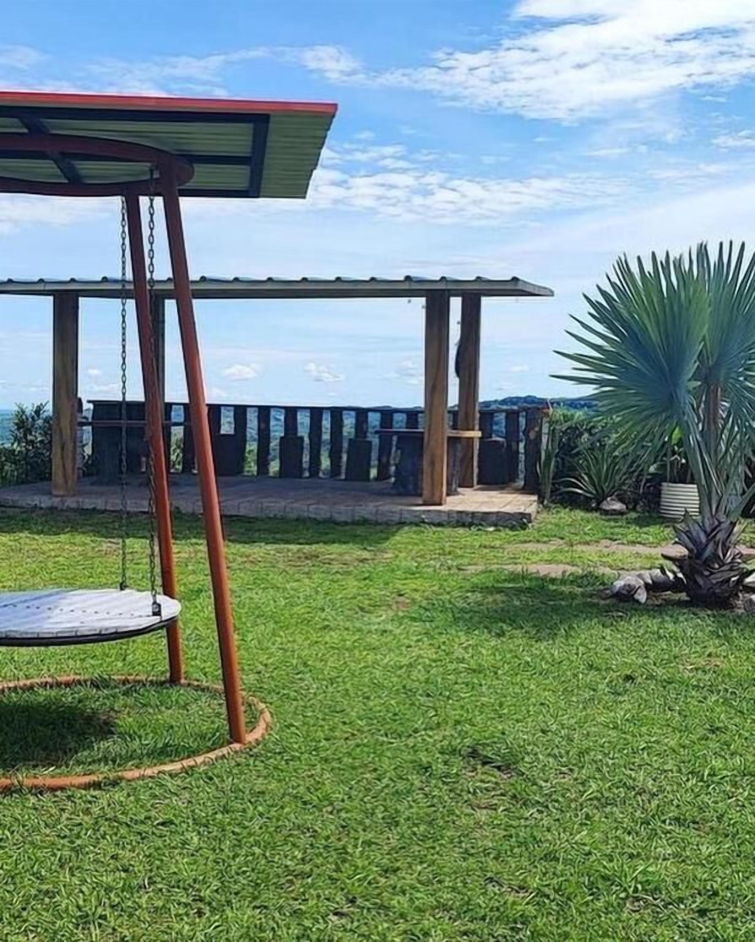A grassy outdoor area with a swing set and a covered seating area.
