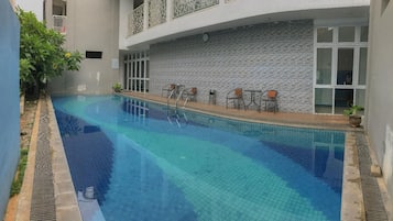 A swimming pool with a tiled edge, surrounded by a low wall and a few chairs.
