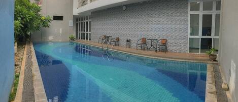 A swimming pool with a tiled edge, surrounded by a low wall and a few chairs.
