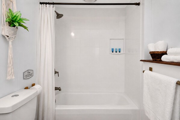 Une salle de bain avec une douche, des toilettes, un lavabo, une plante et une étagère avec des serviettes.