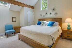 Une chambre à coucher avec un lit en bois, une chaise bleue, une table de chevet avec une lampe et une fenêtre donnant sur des arbres.