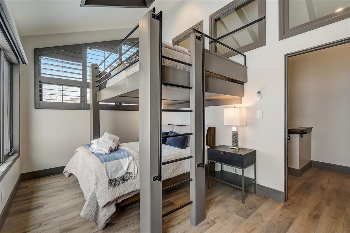 A compact bedroom with a bunk bed, a desk, and a window with blinds.