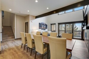 A modern dining area with a wooden table and beige chairs, a staircase, and a balcony with a view of trees. - Lower Deer Valley 4BR | Sleeps 10 | Skier Shuttle | Near Snow Park (Park City)