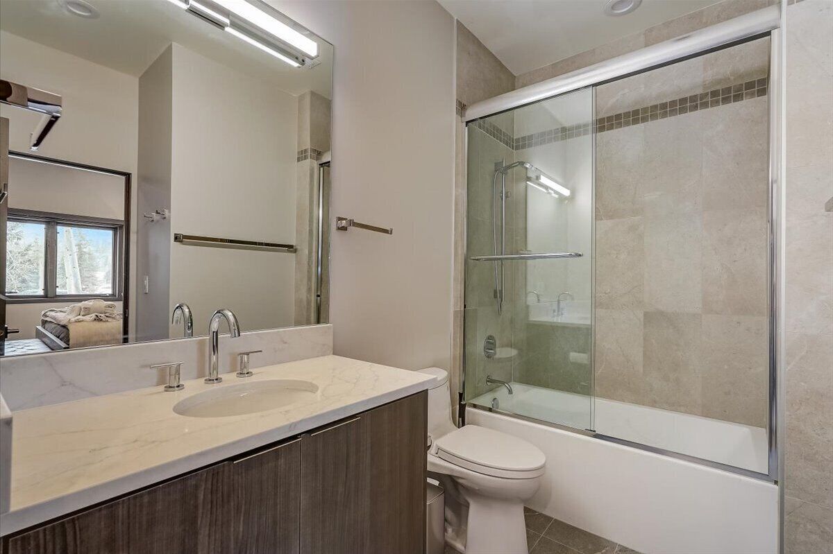 Une salle de bain moderne avec un grand miroir, un lavabo à deux robinets, des toilettes et une douche séparée par une paroi en verre.