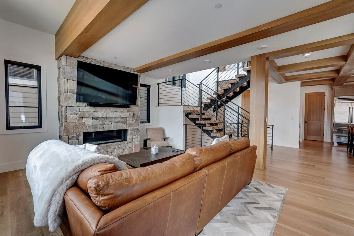 A spacious living room with a stone fireplace, leather sofa, and a staircase leading to another level.