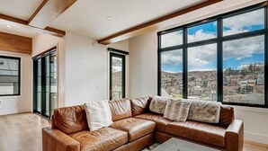 Ein modernes Wohnzimmer mit einer ledernen Eckcouch, einem Couchtisch und großen Fenstern mit Blick auf die Stadt.