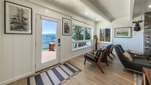 Una habitación amplia con piso de madera, un ventanal con vista al mar y una chimenea de piedra.