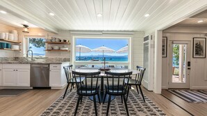 Una cocina con armarios blancos, un lavavajillas de acero inoxidable y un ventanal con vista al mar.