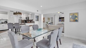 A modern kitchen with white cabinets, a microwave, and a coffee machine. There is a dining area with a glass table and gray chairs. - Wonderful Heated Pool House Delray Beach near Ocean - close to shops and the av’ (Delray Beach)