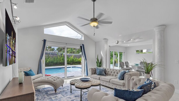 A spacious living room with a large window, a ceiling fan, and a pool visible through the glass doors. - Wonderful Heated Pool House Delray Beach near Ocean - close to shops and the av’ (Delray Beach)