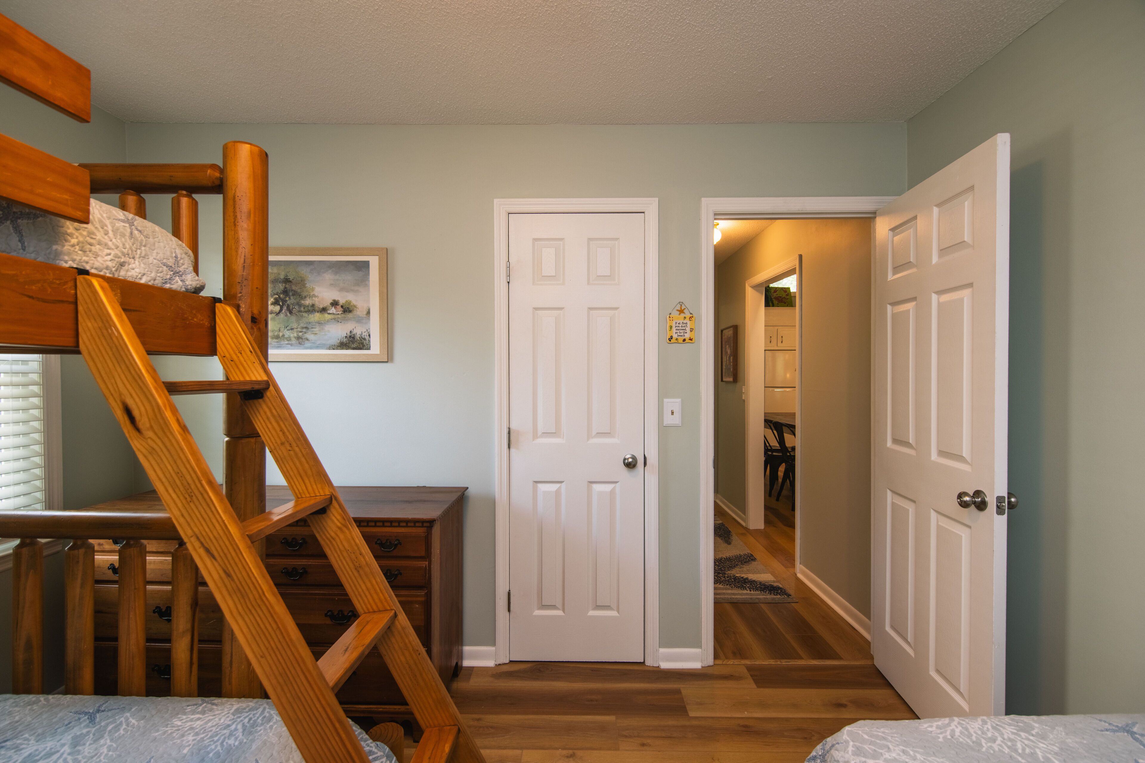 A bedroom with a bunk bed, a wooden dresser, and a door leading to another room.