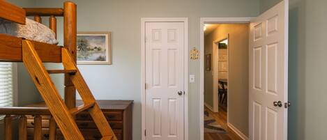 A bedroom with a bunk bed, a wooden dresser, and a door leading to another room.