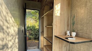 A narrow hallway with wooden walls and a concrete floor, leading to a door. Shelves with decorative items and a small appliance are visible. - Sunset Palm Alojamiento Rural (San Gil)