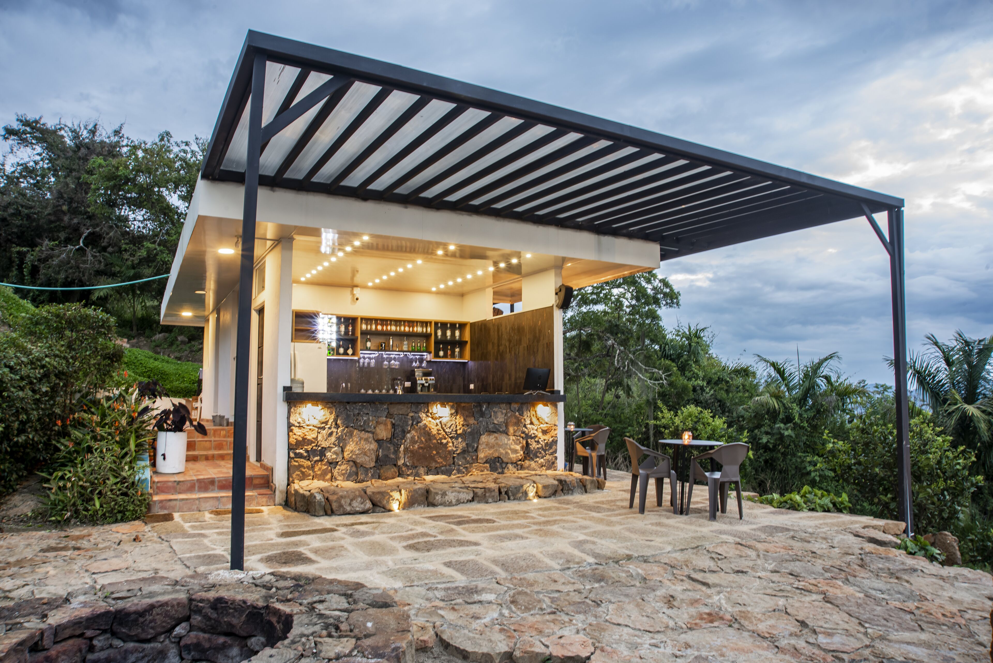 Un área de bar exterior moderna con mostrador de piedra, taburetes y una pérgola.