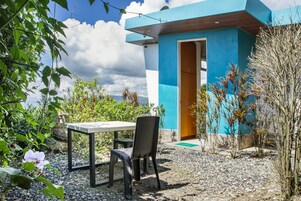 Un edificio moderno con fachada azul, una puerta de madera y una mesa con una silla afuera.
