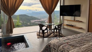 A bedroom with a large window, a TV, a small table with chairs, and a bed. - Sunset Palm Alojamiento Rural (San Gil)