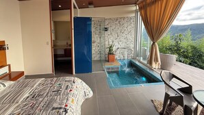 A modern bedroom with a large bed, a small bathroom, a stone wall, a window with curtains, and a view of greenery. - Sunset Palm Alojamiento Rural (San Gil)