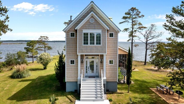 Une maison à deux étages avec un porche à l’avant, un escalier menant à l’entrée et une vue sur le lac.