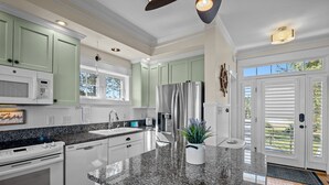Une cuisine moderne dotée de plans de travail en granit, d’appareils électroménagers en acier inoxydable et de meubles de couleur vert clair.